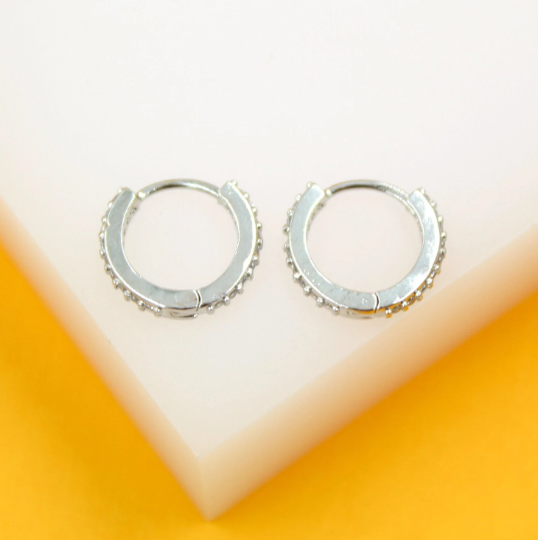 Two silver hoop earrings rest on a white display surface against a vibrant orange background.