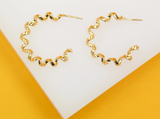 A pair of shiny gold spiral hoop earrings rests on a white and yellow display stand.