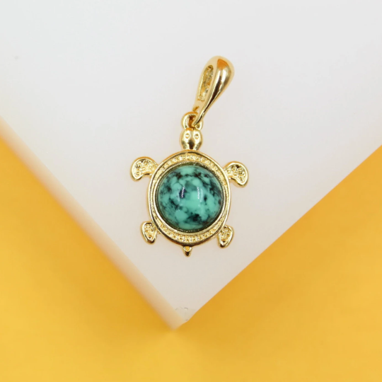 A gold turtle pendant with a turquoise stone shell rests against a white and yellow display background.
