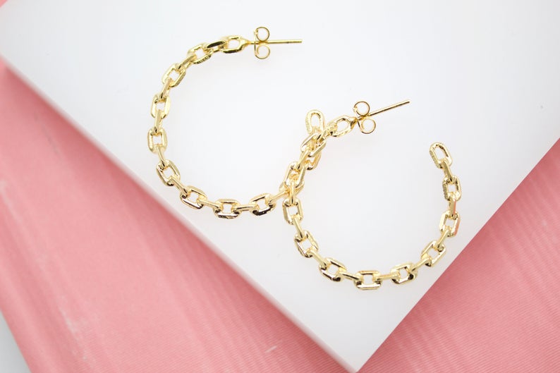A pair of gold chain link hoop earrings rests on a white and pink display surface.