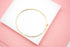 A sleek gold hoop bracelet rests on a white display against a soft pink background.