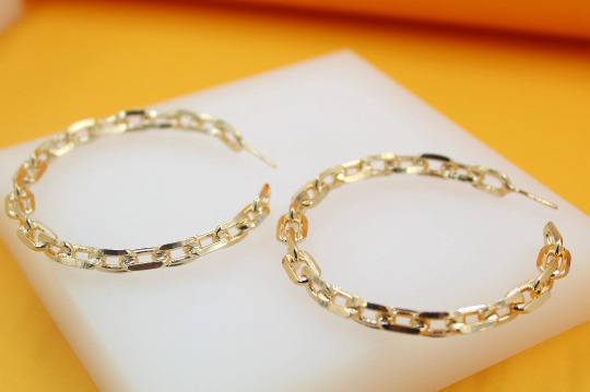 A pair of polished gold-plated hoop earrings with an interlocking chain-link design rests on a white display pad.