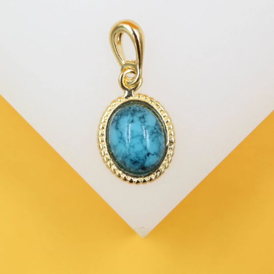 A gold-framed oval turquoise gemstone pendant rests against a white and yellow background.