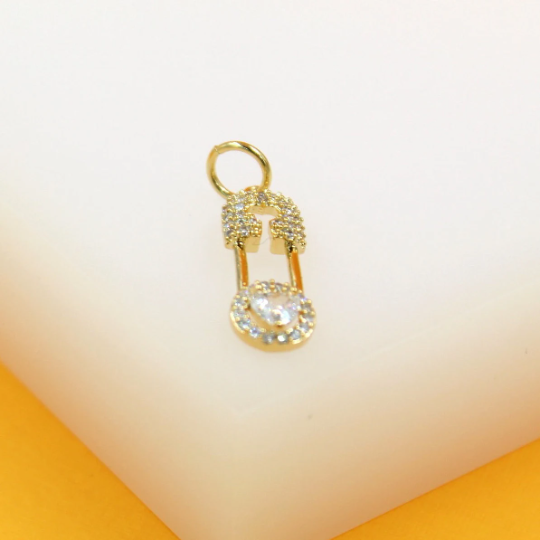 A sparkling gold safety pin charm rests on a white display surface.