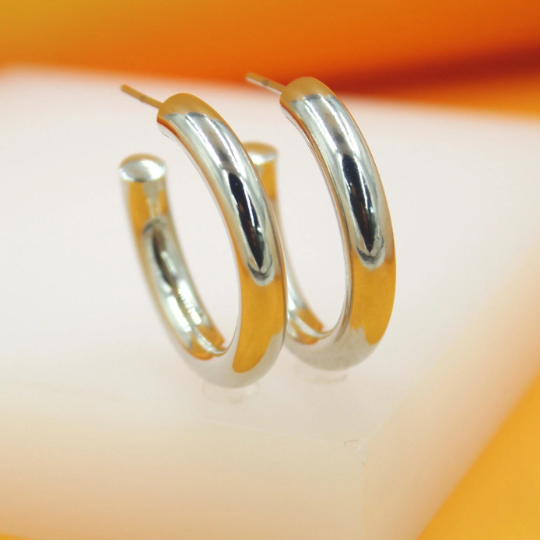 A pair of sleek silver hoop earrings rests upright on a white and orange display stand.