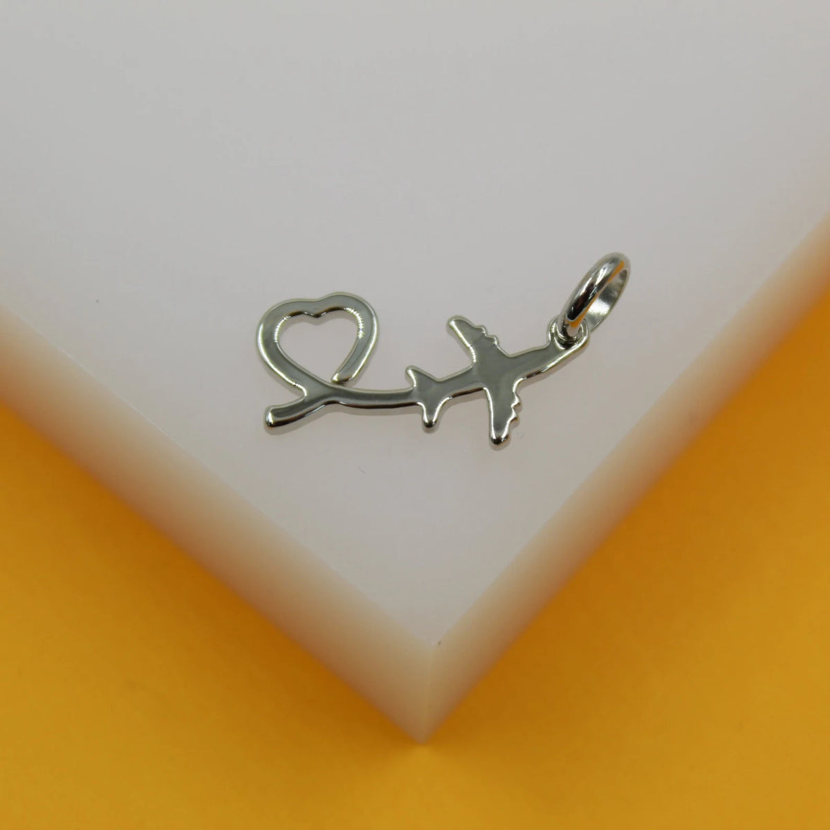 A silver airplane pendant featuring an integrated heart shape rests on a white and yellow display surface.
