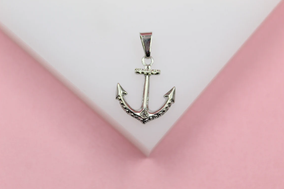 A gleaming silver anchor pendant rests against a soft white and pink background.