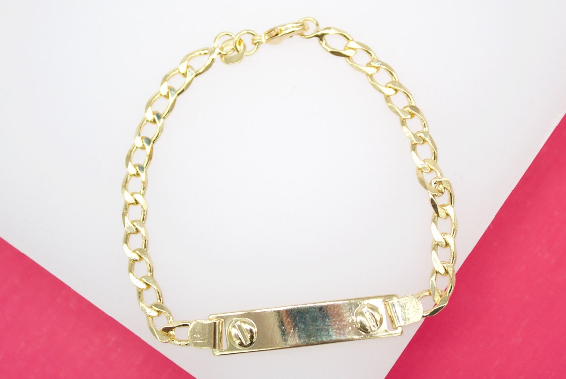A polished gold ID bracelet with a curb chain rests against a vibrant pink and white background.