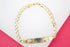 A polished gold ID bracelet with a curb chain rests against a vibrant pink and white background.