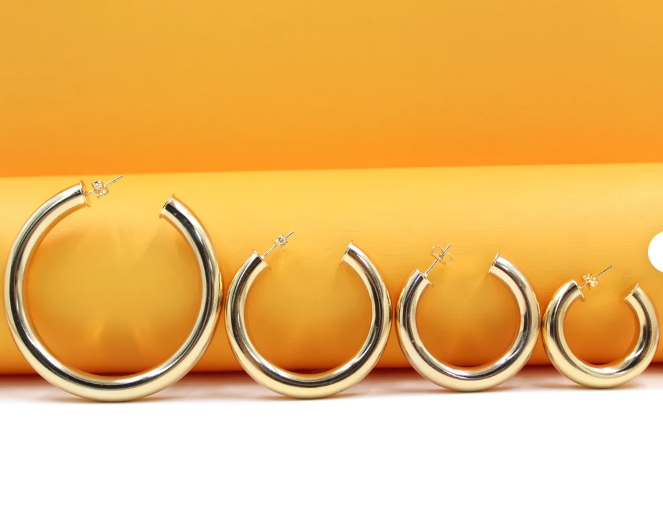 Four thick gold hoop earrings in graduated sizes display their polished finish against a vibrant yellow and white background.