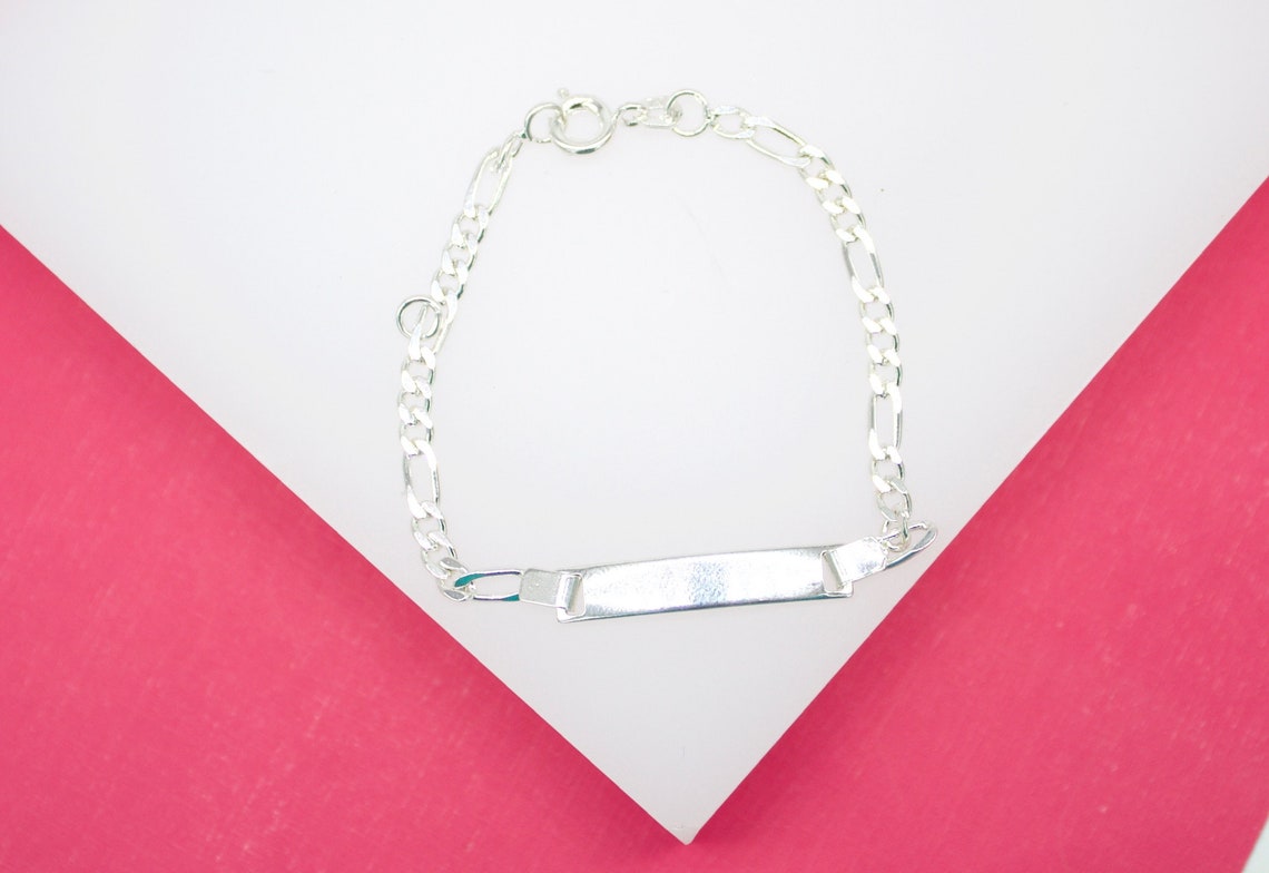 A polished sterling silver ID bracelet rests on a white and pink background, showcasing its glossy nameplate and classic chain links.