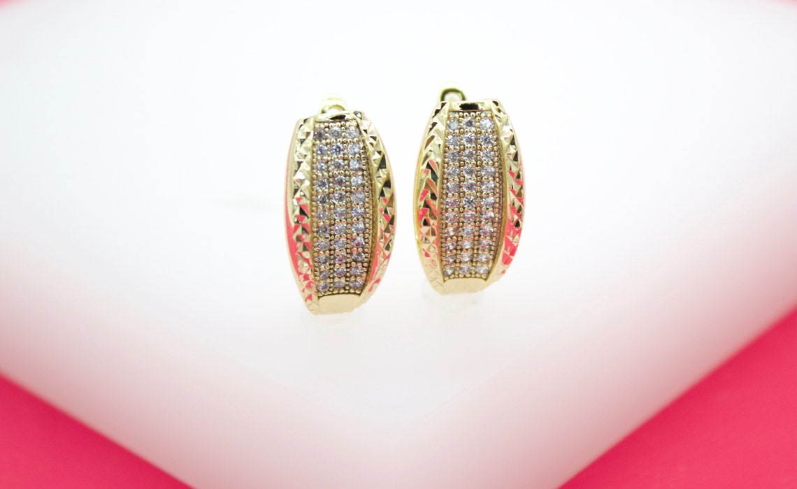 A pair of elegant gold hoop earrings features glittering pave-set cubic zirconia stones down the center and textured geometric patterns along the edges.