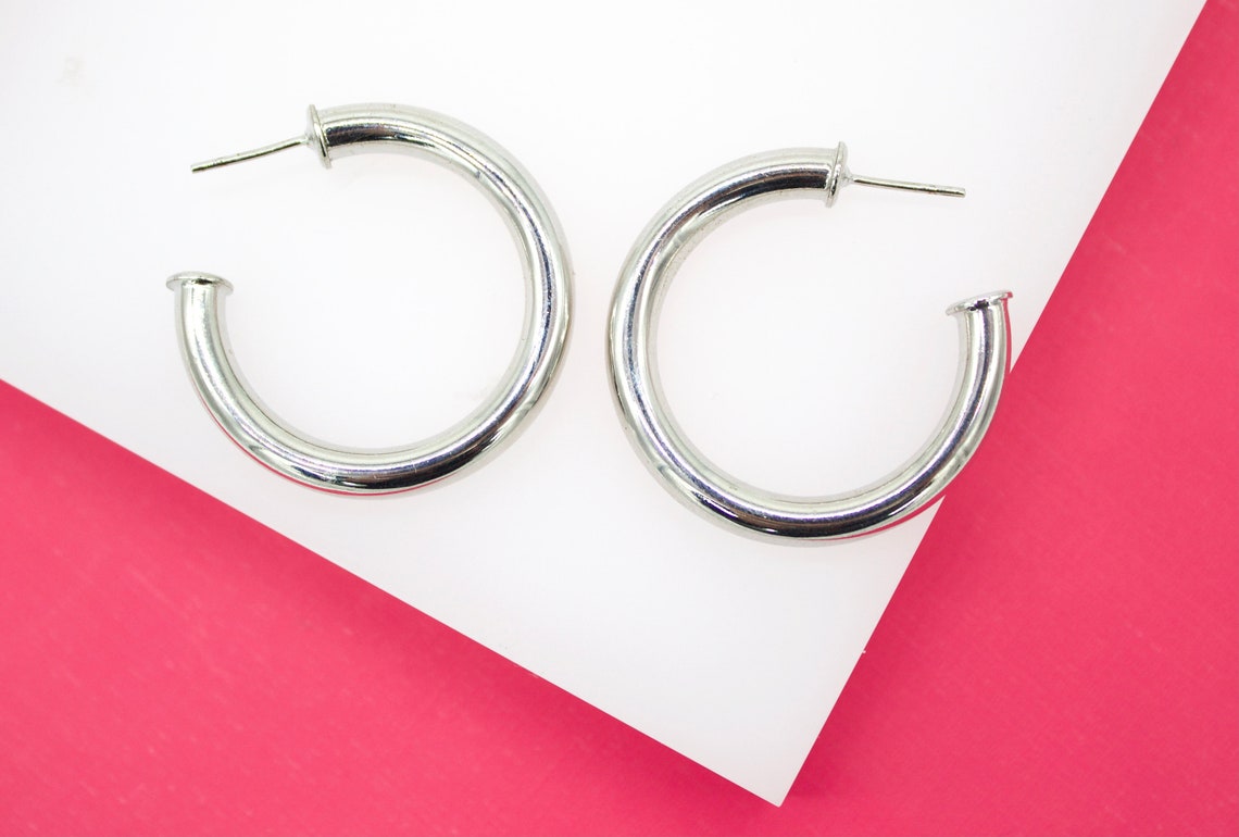 A pair of glossy silver hoop earrings rests on a white and pink display.