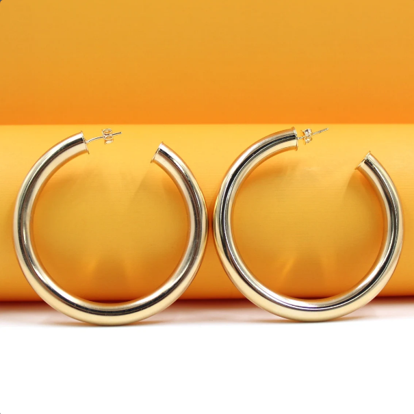 A pair of thick gold hoop earrings rests against a vibrant orange and white background.