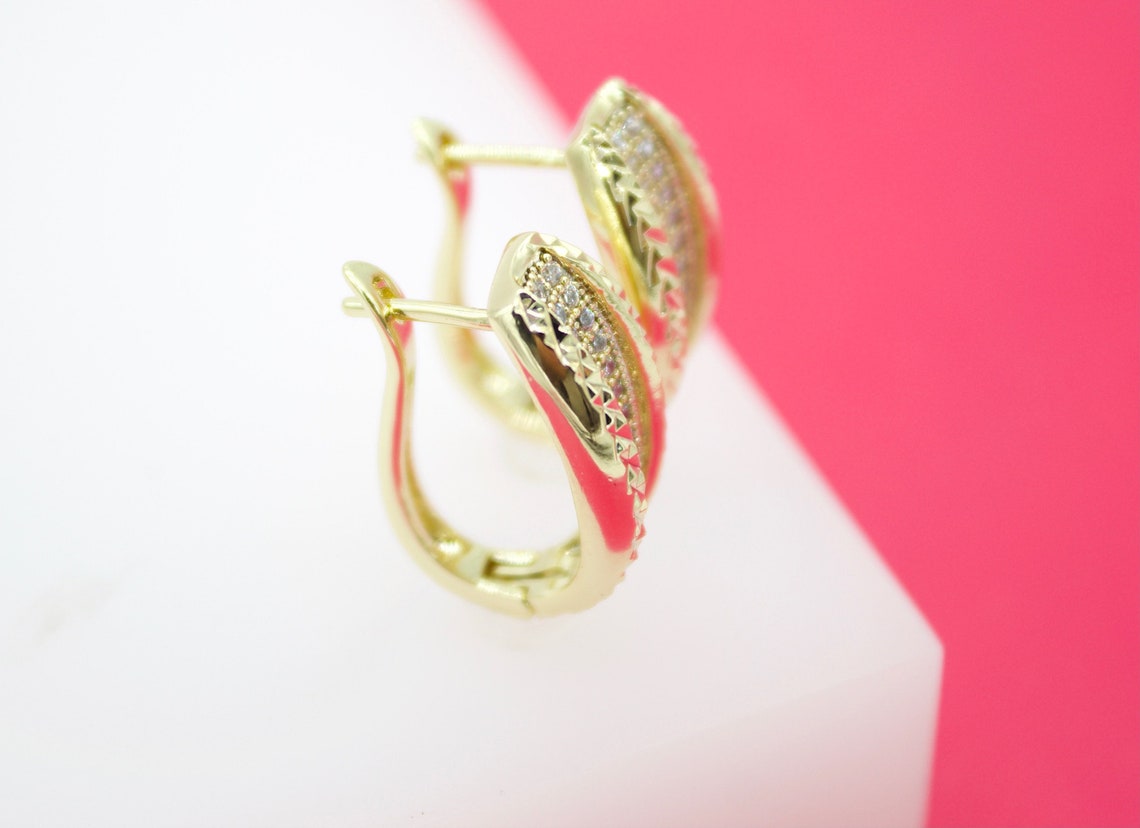 A pair of elegant gold hoop earrings with sparkling cubic zirconia stones rests on a pink and white display surface.