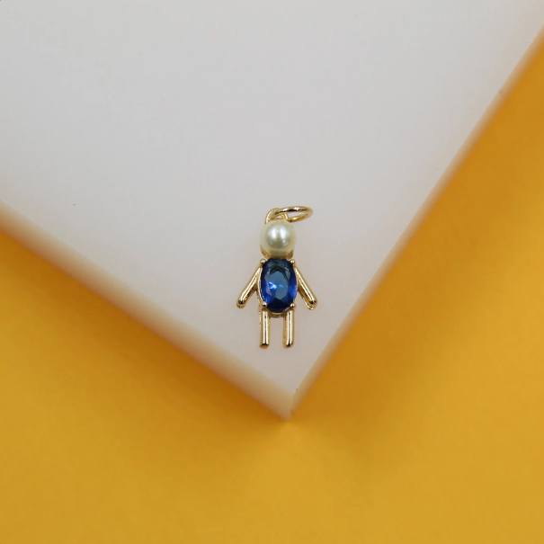 A cute gold boy charm pendant features a pearl head and a sparkling blue crystal body resting on a white display block.