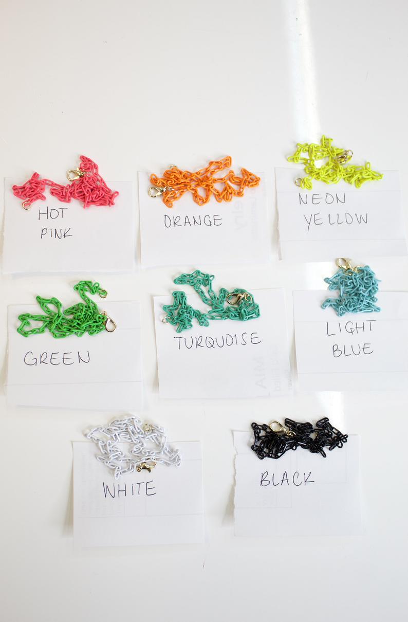 Eight colorful plastic chain necklaces with lobster clasps rest above handwritten paper labels indicating their colors.