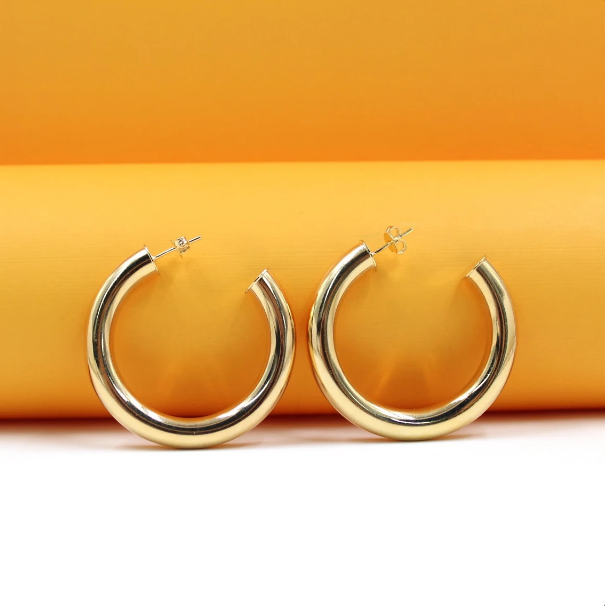 A pair of thick gold hoop earrings rests against a vibrant orange and white background.