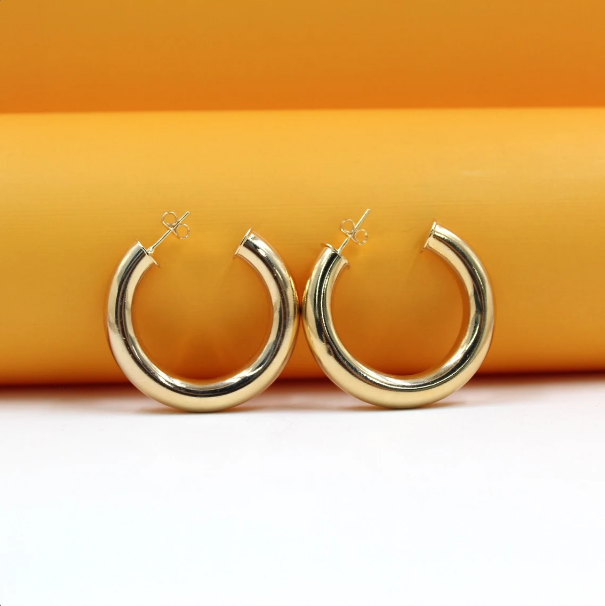 Two polished gold hoop earrings rest against a bright orange and white background.