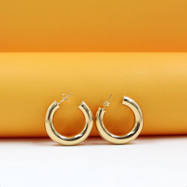 A pair of thick gold hoop earrings rests on a bright orange and white studio background.