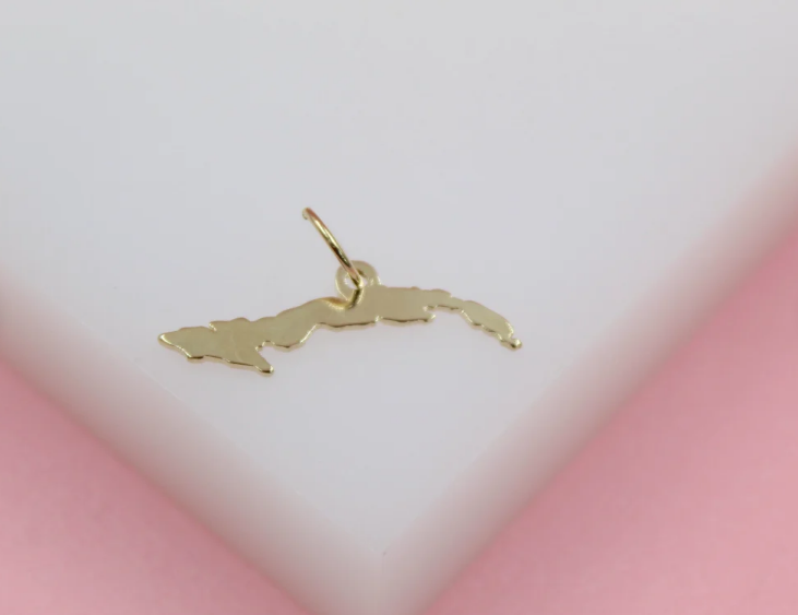 A delicate gold Cuba map pendant rests on a white display surface against a soft pink background.