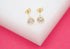 A pair of gold crown-setting stud earrings with sparkling cubic zirconia stones rests elegantly on a white display block against a vibrant pink background.