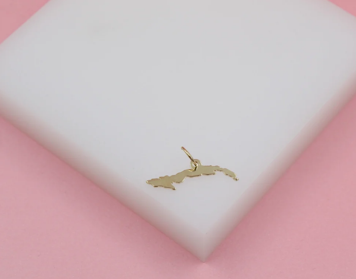 A gold Cuba map charm rests on a white display block against a pink background.