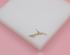 A gold Cuba map charm rests on a white display block against a pink background.