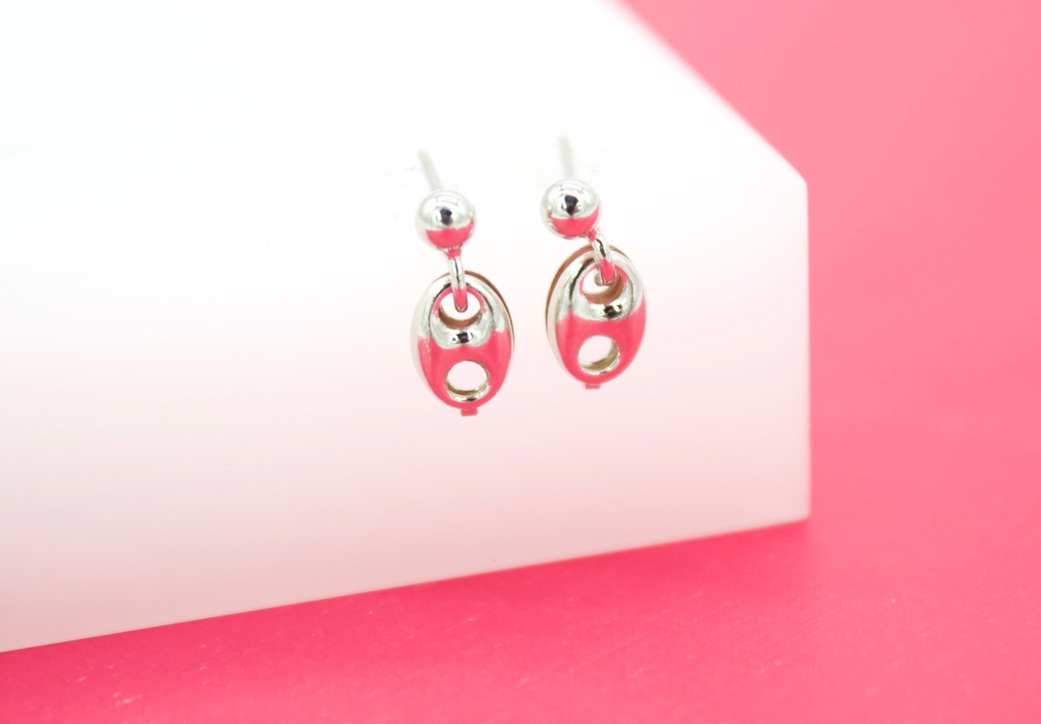 A pair of silver ball-stud dangle earrings featuring glossy pink enamel link charms rests on a white display block against a vibrant pink background.