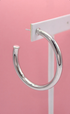 A polished silver hoop earring hangs on a white display card against a soft pink background.