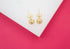 A pair of gold filigree ball stud earrings rests on a white and bright pink background.