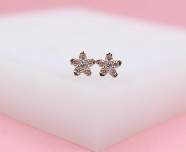 A pair of dainty gold flower stud earrings features sparkling pink crystal petals surrounding clear center stones.