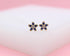 A pair of gold flower stud earrings features dark blue cubic zirconia petals and a clear center stone against a soft white background.