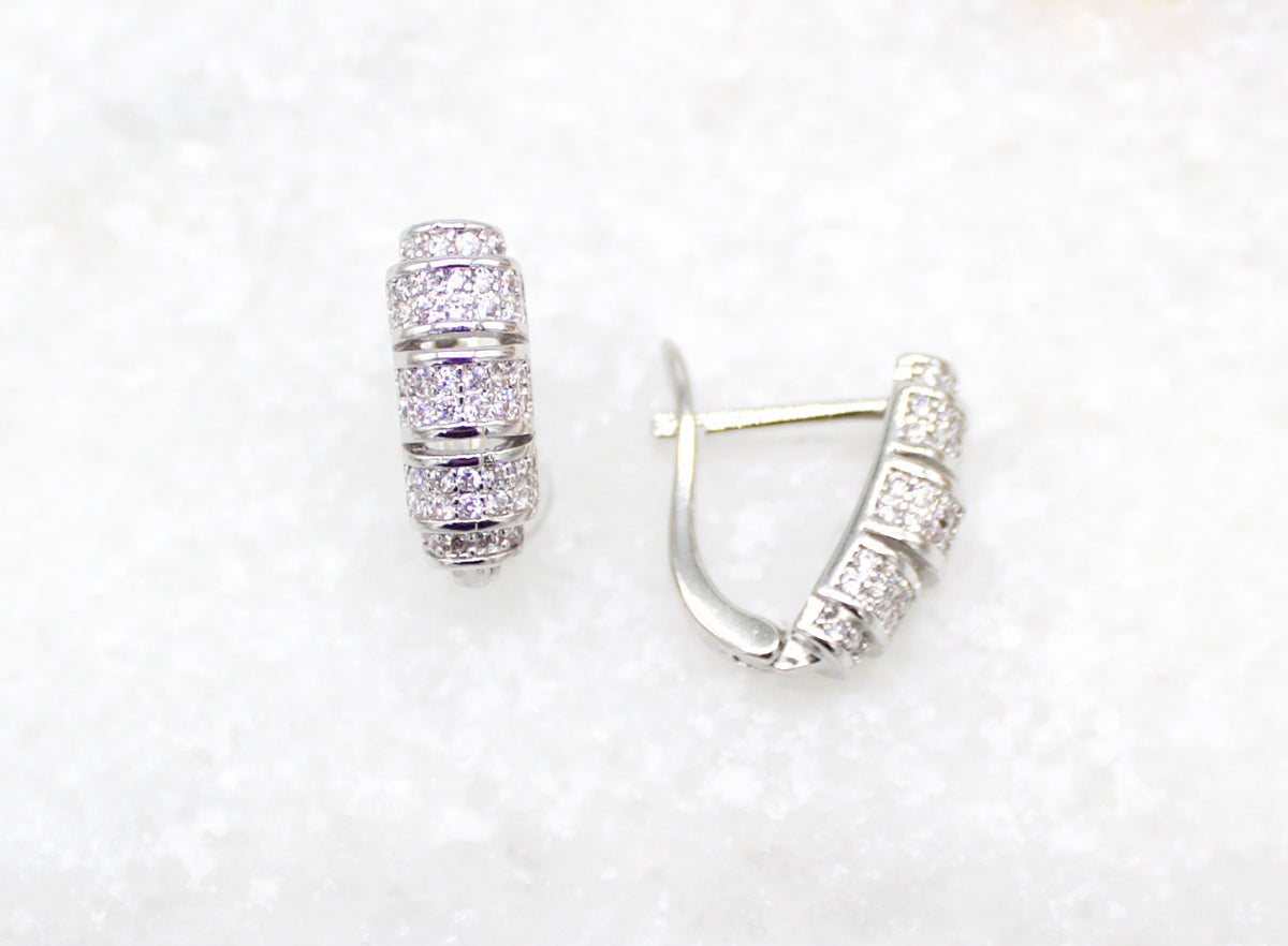 A pair of silver hoop earrings adorned with sparkling cubic zirconia stones rests against a textured white background.