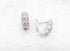 A pair of silver hoop earrings adorned with sparkling cubic zirconia stones rests against a textured white background.