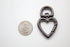A gunmetal heart-shaped swivel lobster clasp lies next to a US quarter coin on a white surface to show its scale.