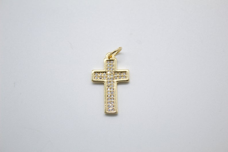 A sparkling diamond-encrusted gold cross pendant rests against a plain grey background.