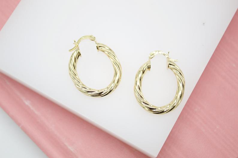 Two twisted gold hoop earrings rest neatly on a white and pink display surface.