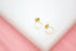 A pair of delicate gold circle stud earrings rests on a white and pink surface.