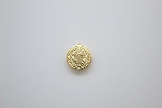A small round gold Saint Benedict medal lies centered on a plain white background.