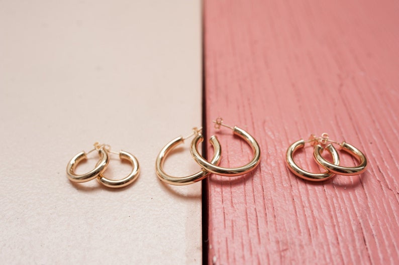 Three pairs of glossy gold hoop earrings in varying sizes rest on a split surface of light pink and textured coral wood.