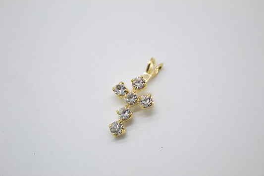 A delicate gold cross pendant embellished with sparkling clear rhinestones rests against a plain white background.
