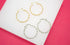 Two gold and two silver twisted hoop earrings rest on a white display surface against a bright pink background.