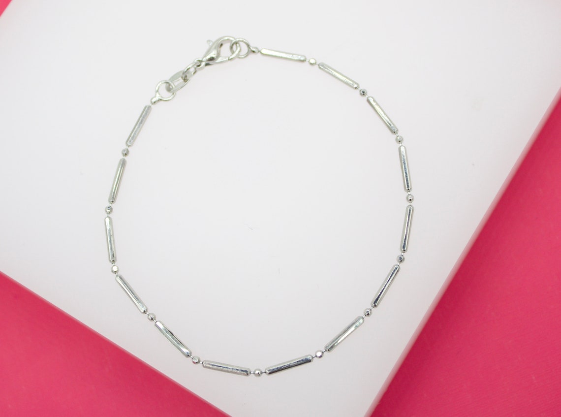 A delicate silver bar and bead anklet rests on a white and pink display surface.