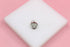 A silver pendant featuring a pavé-set diamond heart rests on a white display block against a soft pink background.
