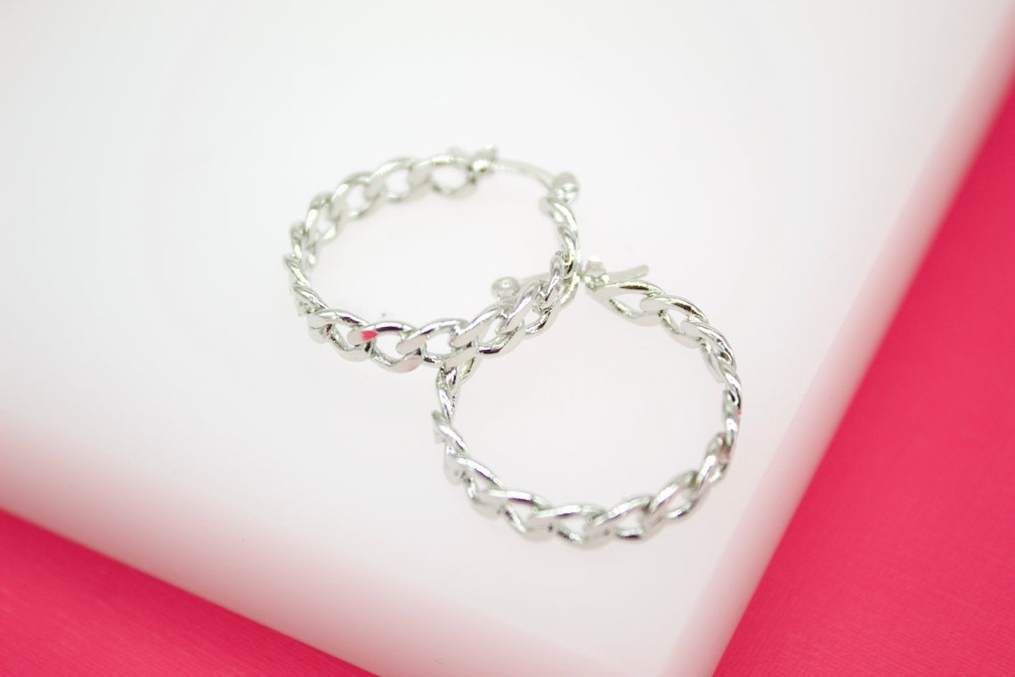 A pair of silver chain-link hoop earrings rests against a white and pink backdrop.
