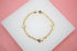 A delicate gold shell charm bracelet rests on a white display surface against a pink background.