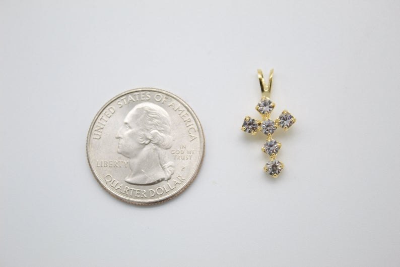 A small gold cross pendant adorned with sparkling cubic zirconia stones rests next to a US quarter coin for scale.