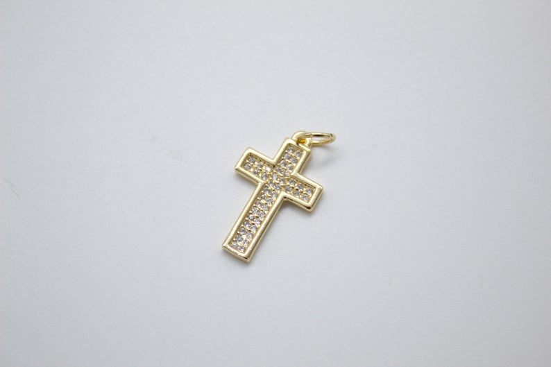 A gold cross pendant encrusted with sparkling cubic zirconia stones lies on a neutral surface.