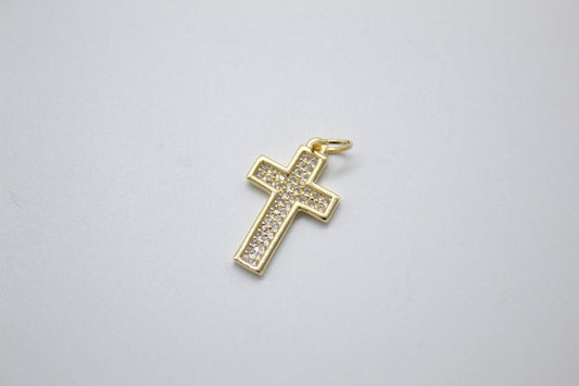 A gold cross pendant encrusted with sparkling cubic zirconia stones lies on a neutral surface.